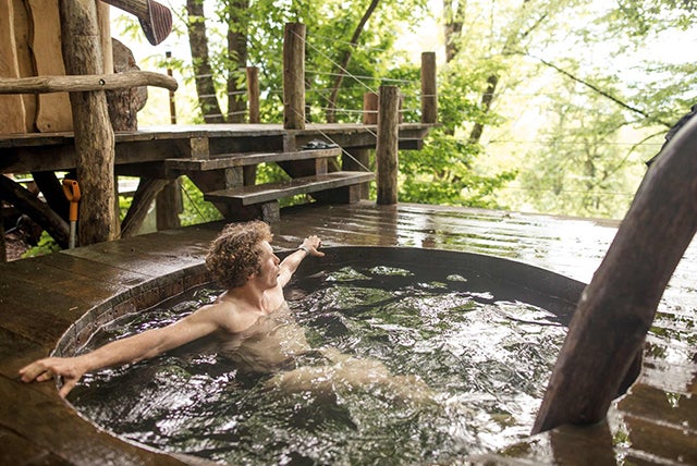 Muž relaxuje ve venkovní dřevěné kádi s dřevěnou terasou a rustikálním schodištěm