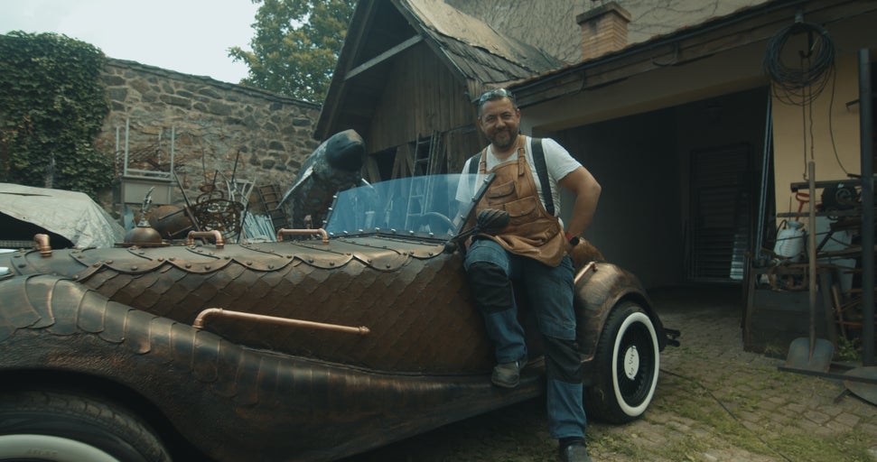 Muž v montérkové zástěře se opírá o automobil na zakázku v Steampunk stylu