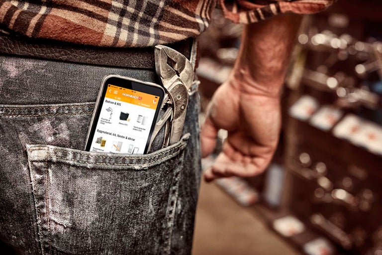 Smartphone s otevřenou aplikací Hornbach, umístěný v kapse džínů s kleštěmi