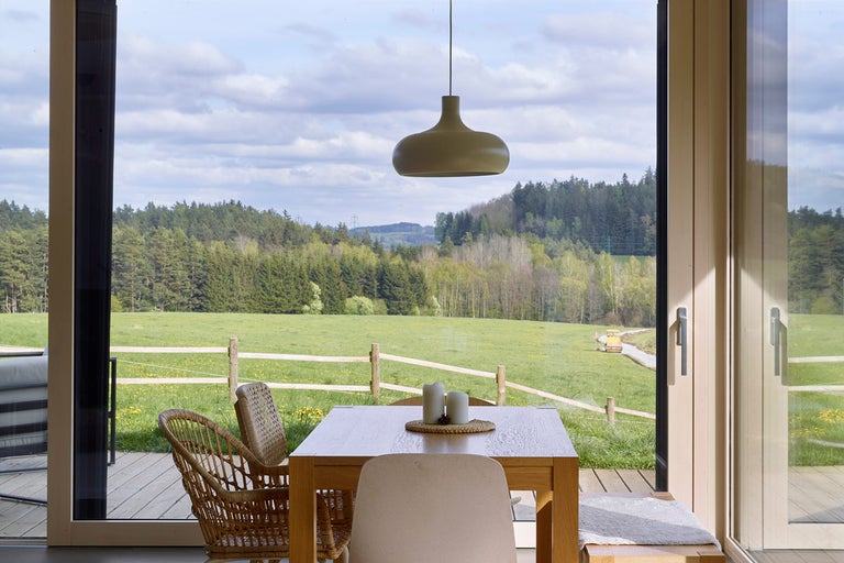 Světlá jídelna s dřevěným stolem, židlemi a výhledem na zelenou krajinu