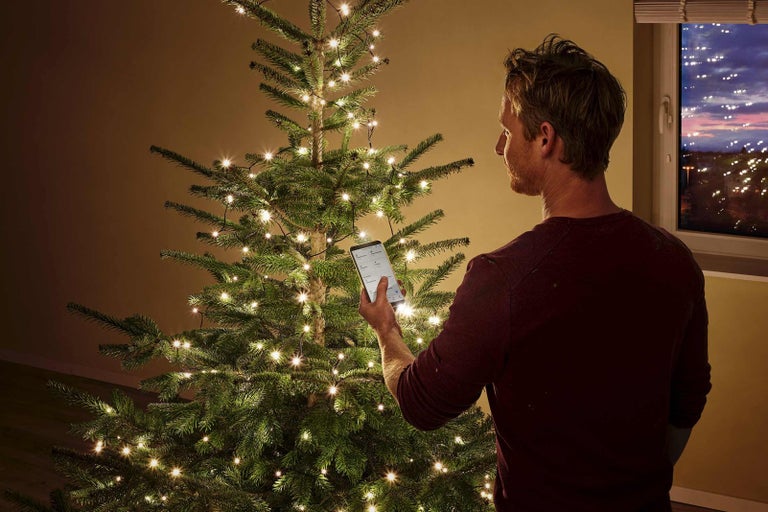 Muž ovládá světelný řetěz na vánočním stromku pomocí smartphonu.