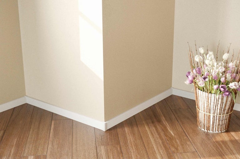 Roh místnosti s bílými podlahovými lištami, dřevěnou podlahou a kyticí květin
