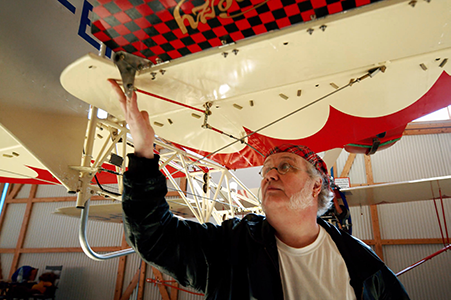 Muž kontroluje letadlo v hangáru. Letadlo má červeno-bílý design.