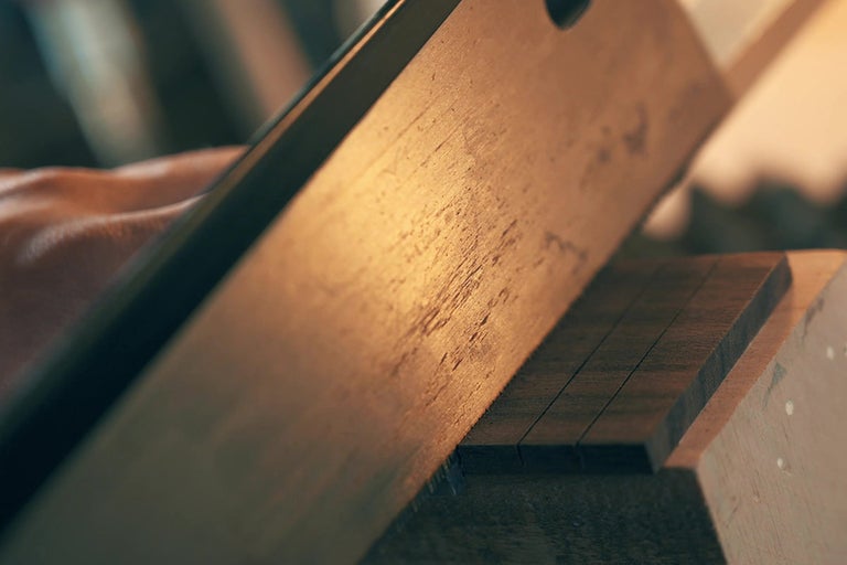 Řemeslník řeže dřevěnou lištu ruční pilou