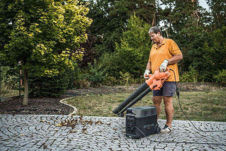 Osoba používá foukač listí vedle napájecí stanice EcoFlow pro zahradnické práce.