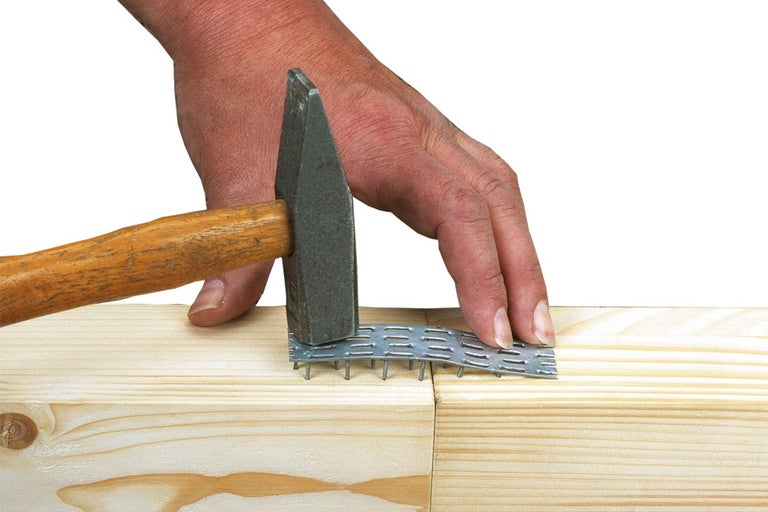 Muž připevňuje hřebíkovou desku kladivem ke dvěma kusům dřeva.