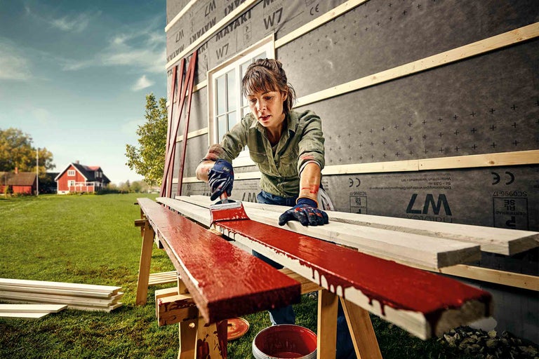 Žena natírá venku dřevěné desky štětcem. Renovace domu na zahradě.