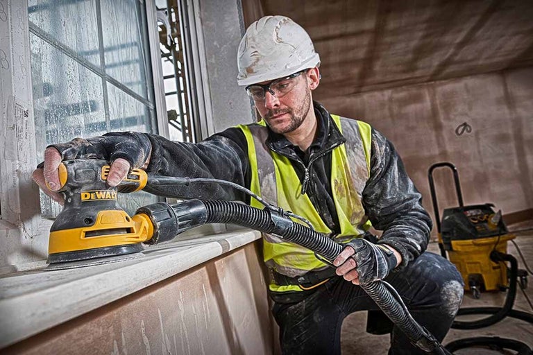 Řemeslník brousí okno excentrickou bruskou DeWalt, připojené odsávání prachu