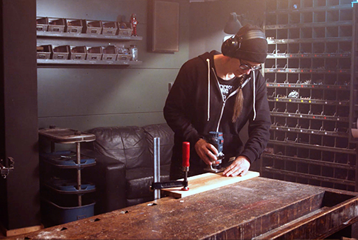 Muž frézuje dřevěnou desku horní frézkou v dílně