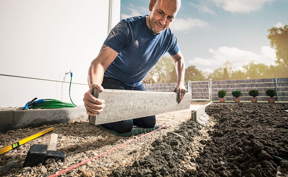 Muž pokládá betonové obrubníky na zahradě