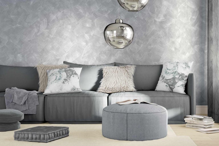 Obývací pokoj s šedou pohovkou, polštáři, pufem a stříbrnou nástěnnou dekorací.