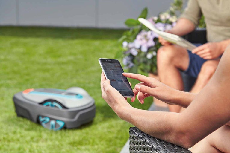 Osoba ovládá robotickou sekačku pomocí aplikace na zahradě.