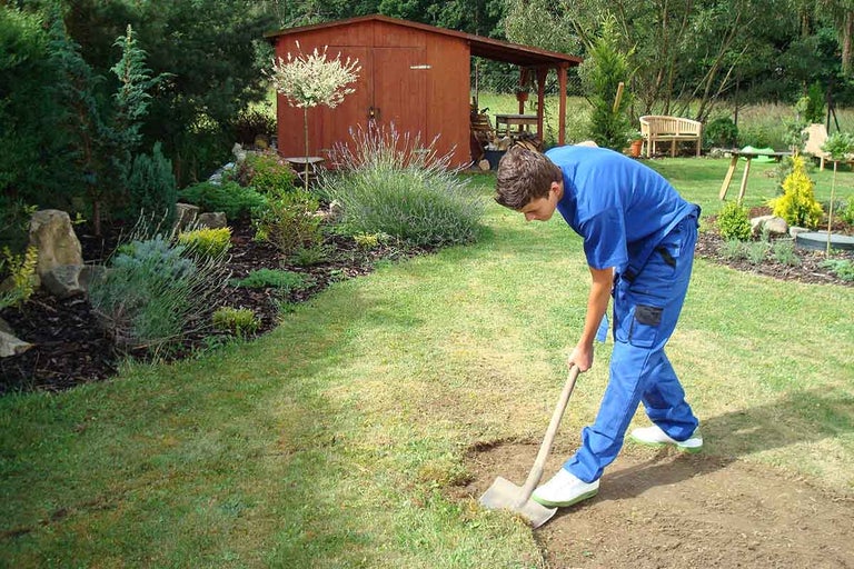 Krajinný snímek s mužem pracujícím v zahradě s rýčem.