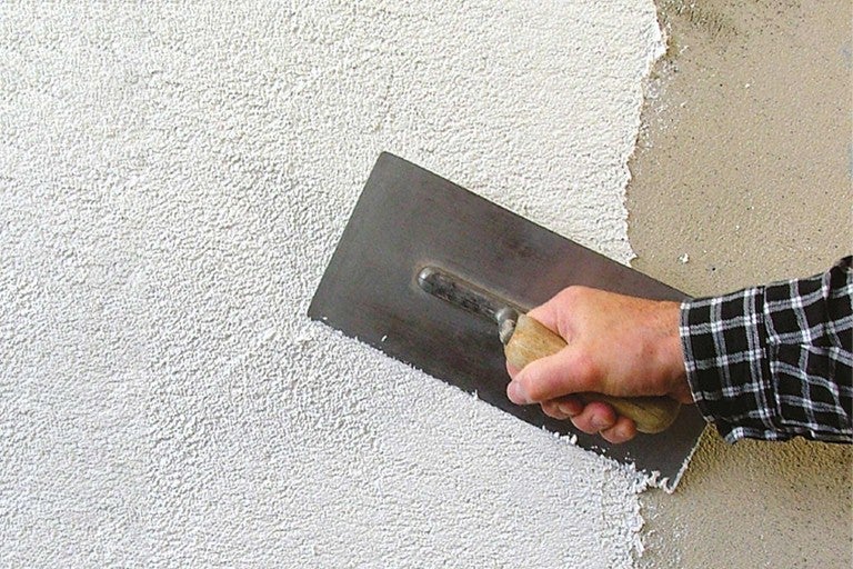 Řemeslník nanáší omítku na stěnu pomocí hladítka.