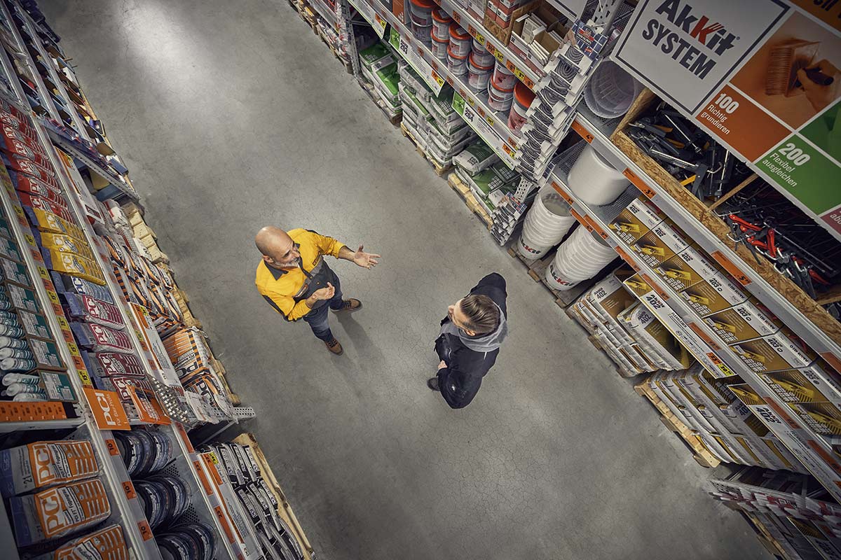 Pohled shora na regál v obchodě pro kutily se dvěma lidmi v uličce.