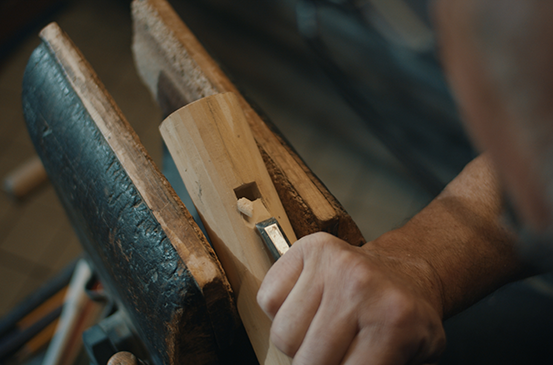 Řemeslník opracovává kus dřeva dlátem v pracovním stole