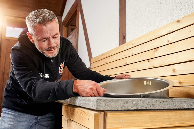 Muž instaluje umyvadlo do zahradního stolu