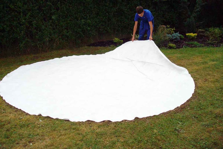 Muž rozkládá bílý kryt bazénu na trávníku