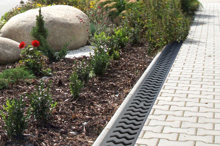 Zahradní krajina s odvodňovacím žlabem vedle chodníku