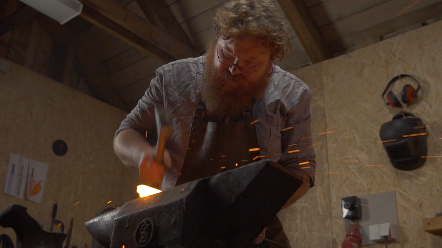 Kovář opracovává žhavý kov kladivem na kovadlině.