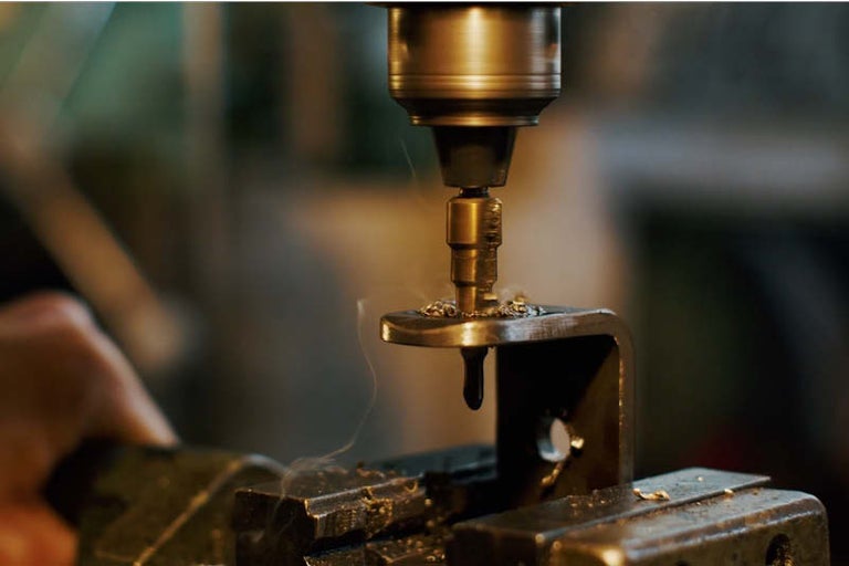 Detailní záběr vrtačky vrtající skrz kov ve svěráku.