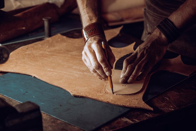 Řemeslník tužkou obkresluje tvar na kusu kůže.