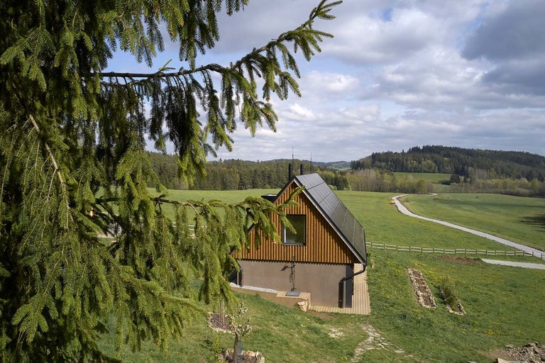 Moderní dům s dřevěnou fasádou a solárním systémem ve venkovském prostředí.