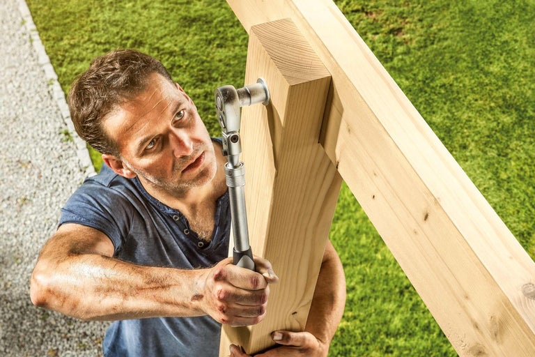 Muž upevňuje dřevěnou konstrukci klíčem na zahradě