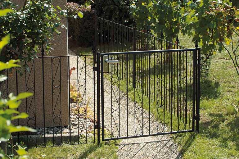Otevřená kovová zahradní branka s klikou v zahradním prostředí