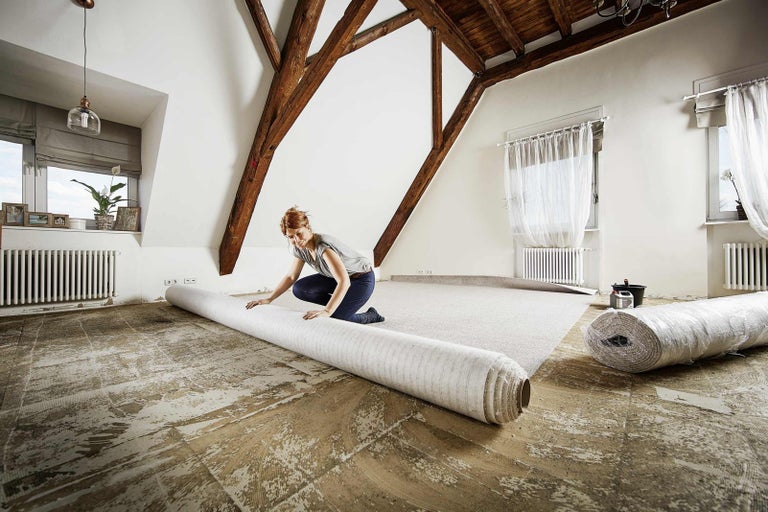 Žena pokládá koberec v místnosti s dřevěným trámovým stropem