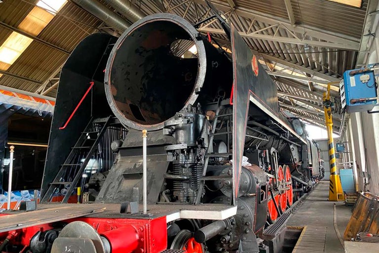 Detail staré černé parní lokomotivy v údržbářské hale.