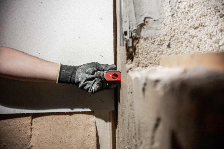 Ruka s ochrannou rukavicí používá laser pro montáž na stěnu.