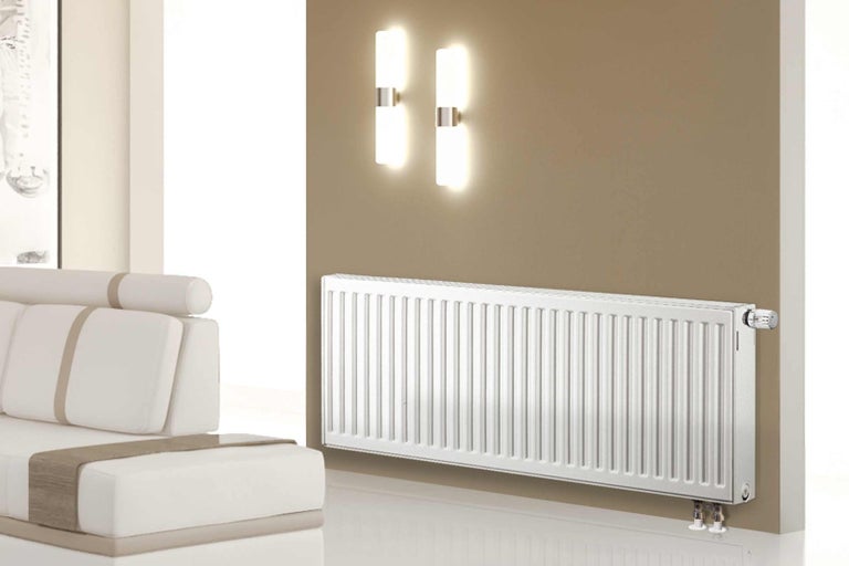 Bílý deskový radiátor namontovaný na zdi v místnosti