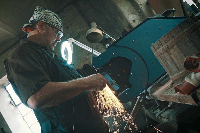 Muž brousí kovový kus s bruskou, z které létají jiskry