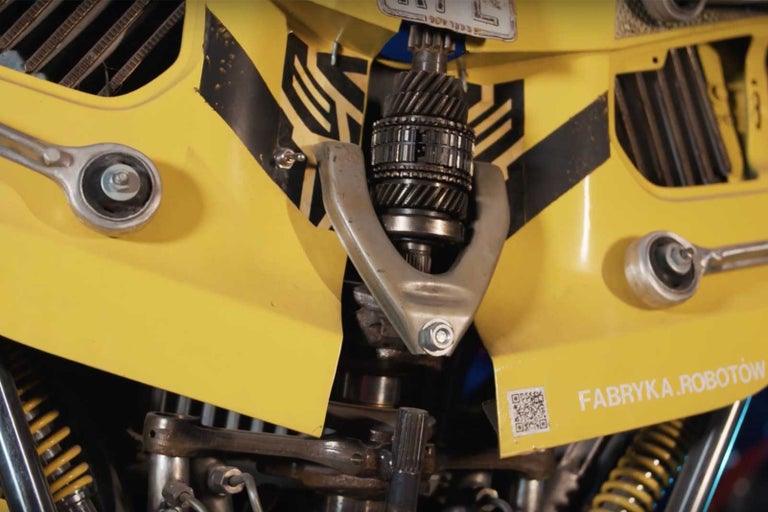 Detailní pohled na sochu vyrobenou ze žlutých a kovových dílů, včetně ozubených kol a klíčů.