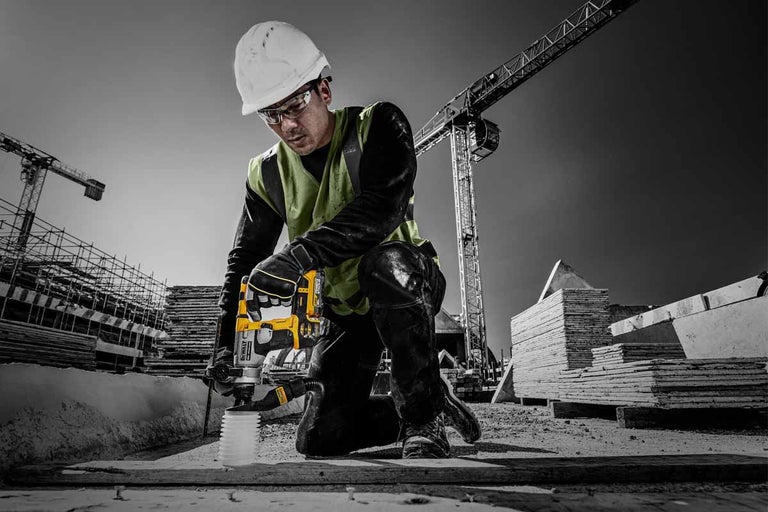 Stavební dělník s ochrannou helmou a brýlemi pracuje s vrtačkou DeWalt na staveništi