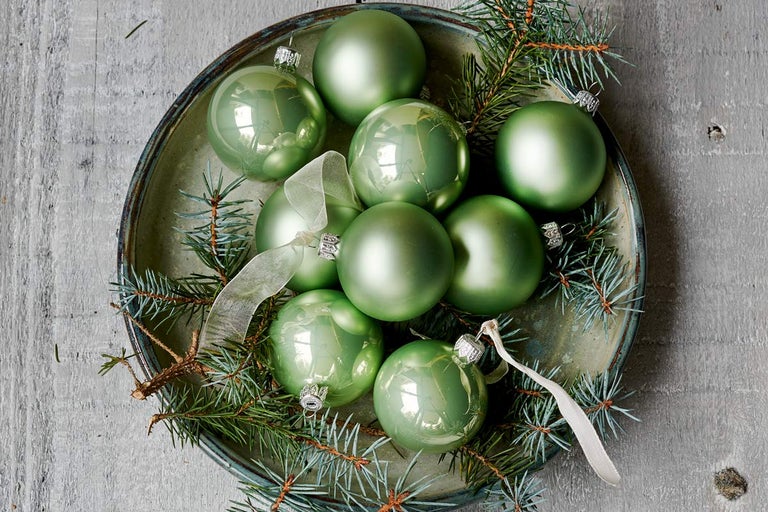 Zelené vánoční koule v misce s větvemi jedlí a stuhami