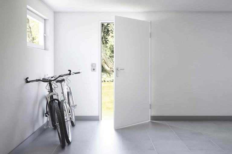 Světlá místnost s otevřenými dveřmi, oknem a jízdními koly na zdi