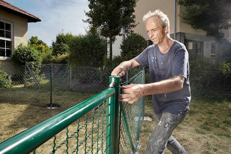 Muž montuje pletivový plot na zahradě.