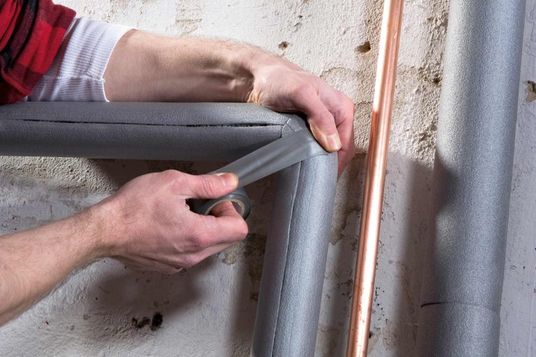 Osoba izoluje topné trubky izolační páskou.