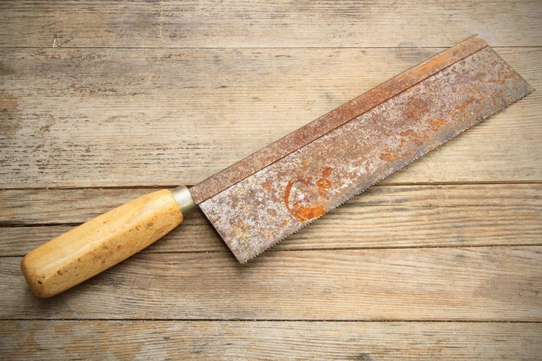 Ruční pila s dřevěnou rukojetí a rzí na dřevěném pozadí