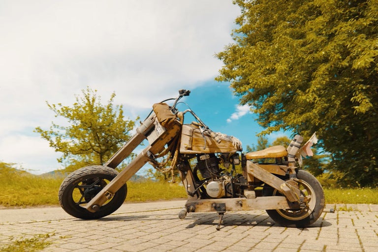 Dřevěná motorka na dlážděné cestě před stromy a modrou oblohou