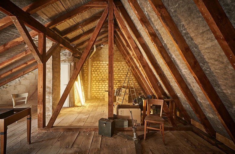 Půda s dřevěnými trámy, cihlovými stěnami, žebříkem a různými předměty.