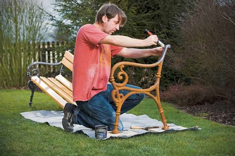Muž natírá lavičku v zahradě štětcem