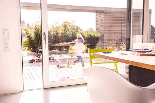 Pohled skrz otevřené balkonové dveře na terasu s hrajícím si dítětem
