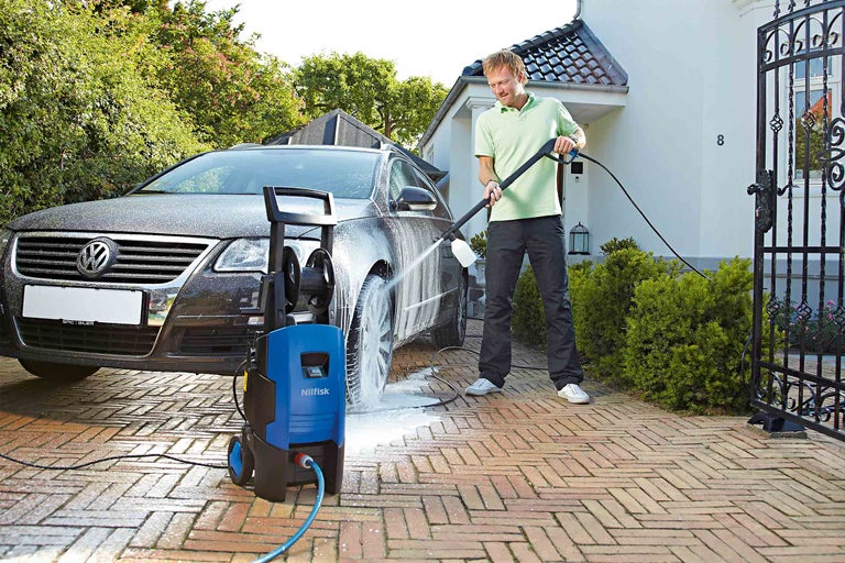 Muž čistí auto vysokotlakým čističem Nilfisk na příjezdové cestě