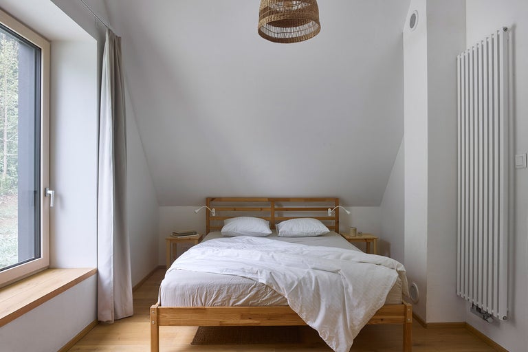 Ložnice s dřevěnou postelí, nočními stolky a radiátorem pod stropní lampou