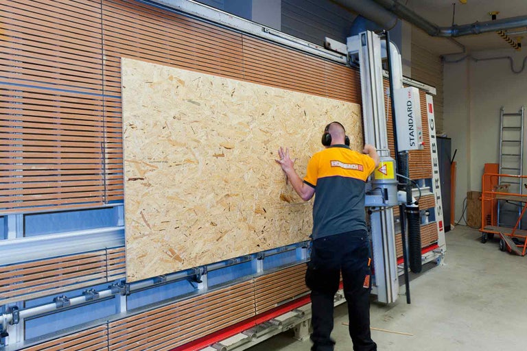 Zaměstnanec společnosti Hornbach opracovává dřevěnou desku pomocí pilového stroje.