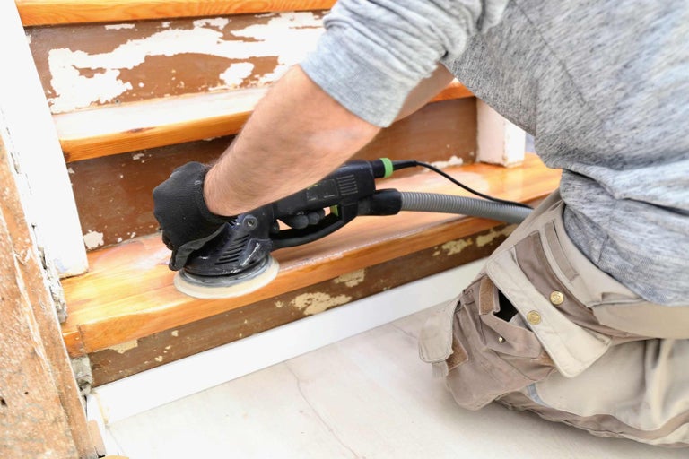 Řemeslník brousí dřevěné schodiště bruskou