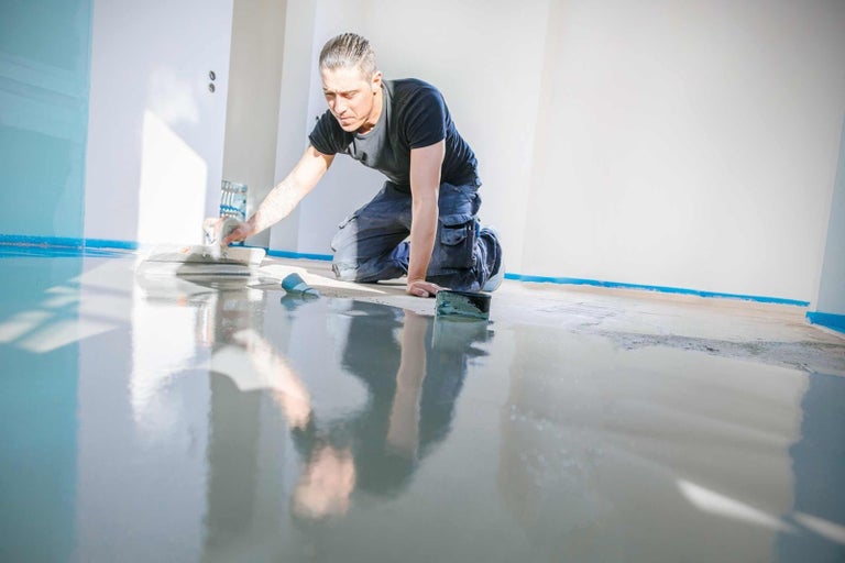 Řemeslník zpracovává potěr s hladítkem v místnosti.